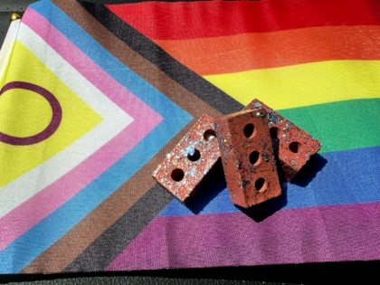 The Progress Pride Flag with a small pile of three bricks on it