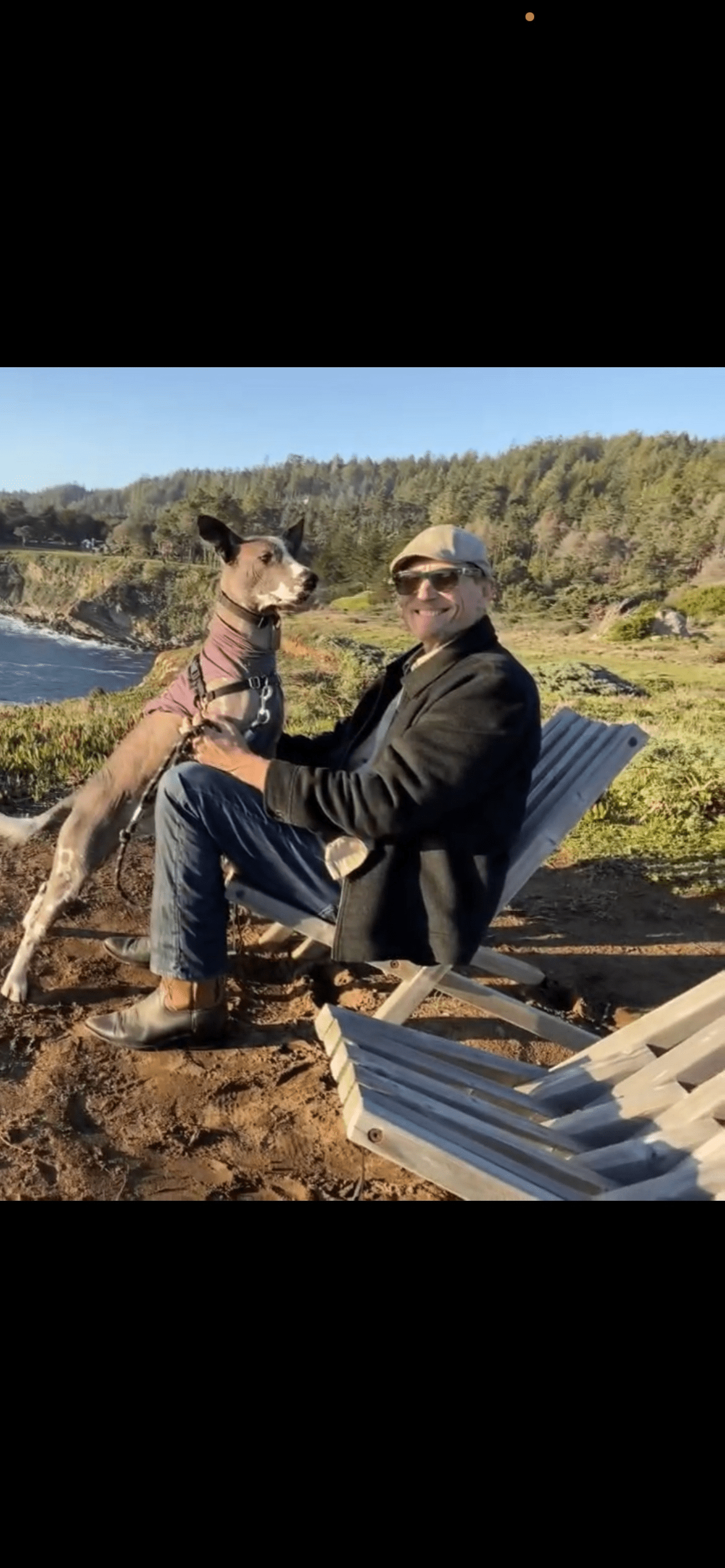 Martin Todd is sitting in a camping chair on a hilltop while a cute dog stands on his lap, overshadowing him